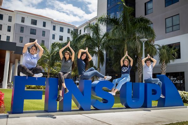 NSU students sitting on giant letters that read "FINS UP!" on campus