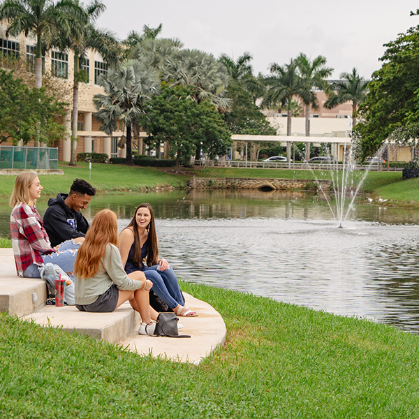 NSU students seated on steps around the NSU Gold Circle Lake, the NSU Library is in the background